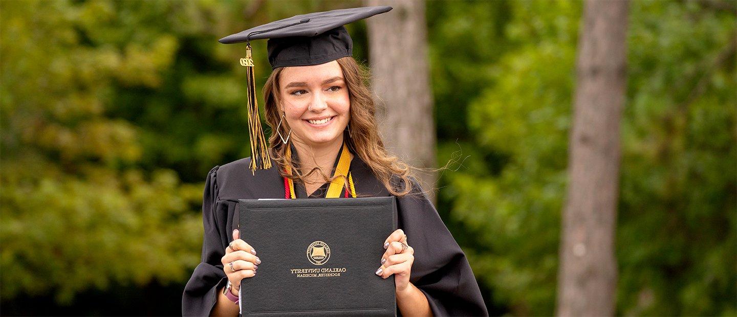 一位十大菠菜台子的女毕业生，戴着帽子，穿着长袍，手里拿着一张文凭.